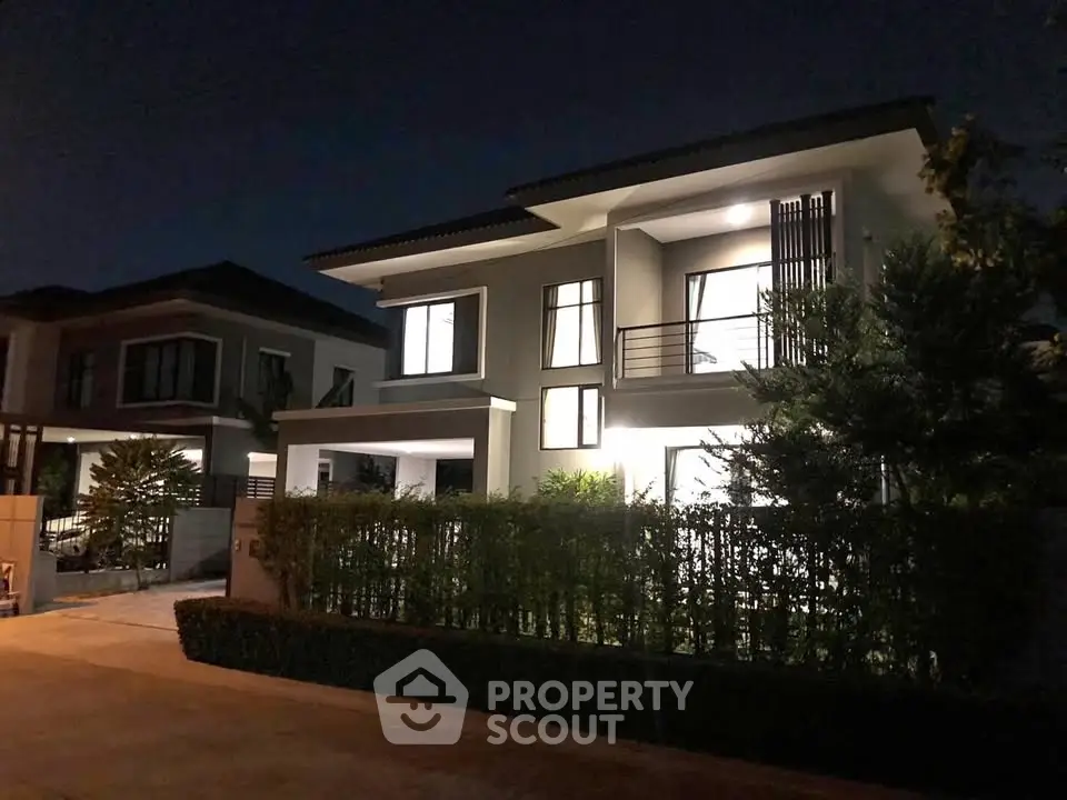 Modern two-story house with illuminated windows and lush greenery at night.
