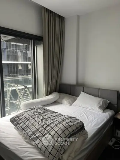 Modern bedroom with large window and city view, featuring a cozy bed and stylish decor.