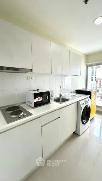 Modern kitchen with sleek white cabinets, washing machine, and microwave in a bright apartment.