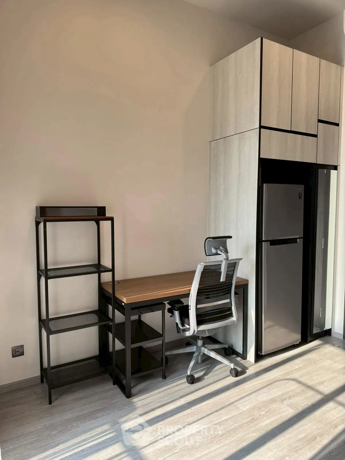 Modern study area with sleek desk, chair, and storage beside a compact fridge in a bright room.