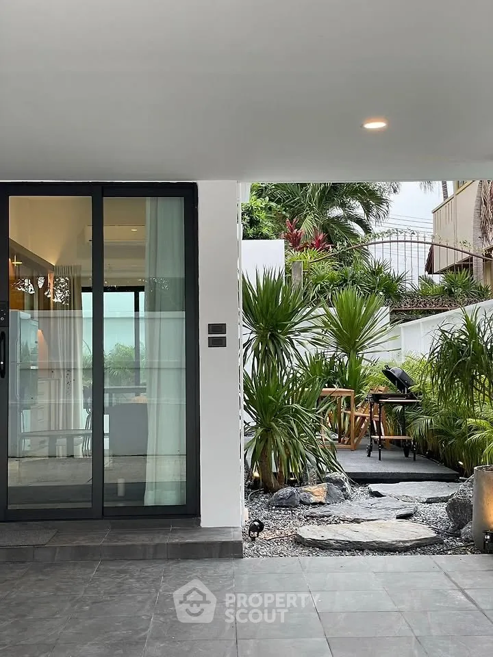 Modern home with glass doors opening to a lush garden and outdoor seating area.