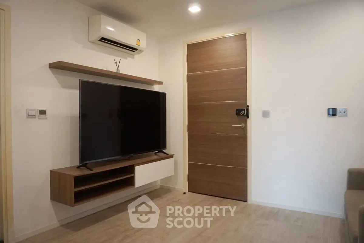 Modern living room with wall-mounted TV and air conditioning unit, featuring sleek wooden flooring and door.