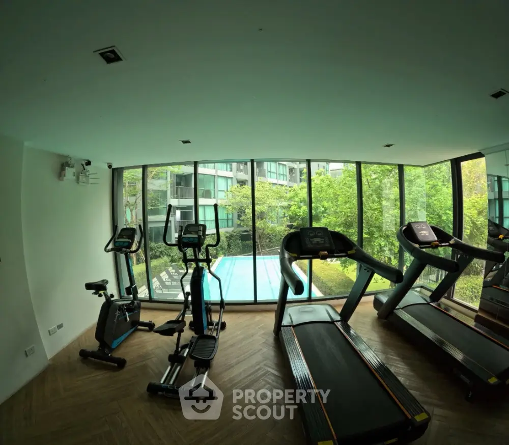 Modern gym with large windows overlooking a pool and garden, featuring treadmills and exercise equipment.