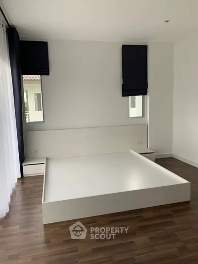 Modern minimalist bedroom with sleek white bed frame and wooden flooring