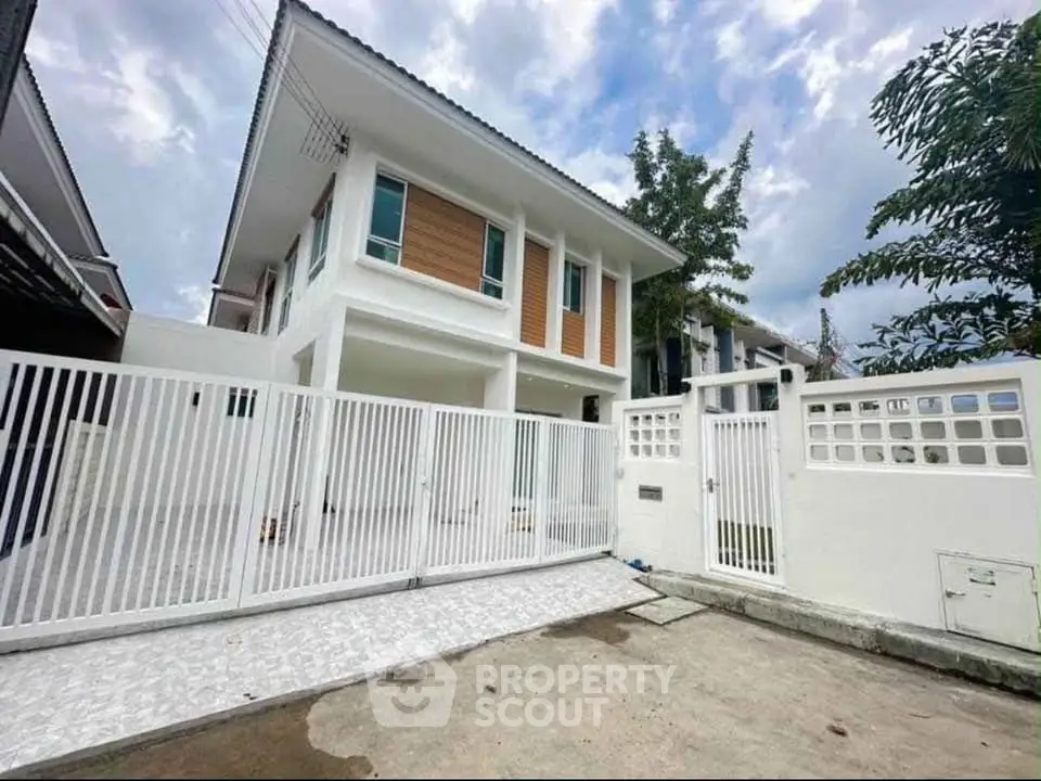 Modern two-story house with white facade and gated entrance in a suburban neighborhood.