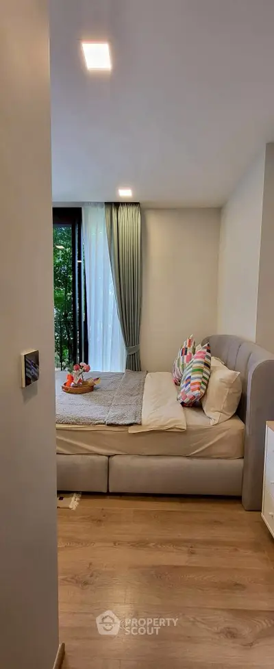 Cozy bedroom with stylish decor and large window offering natural light and garden view.