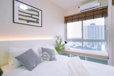 Modern bedroom with large window and city view, featuring stylish decor and cozy seating area.
