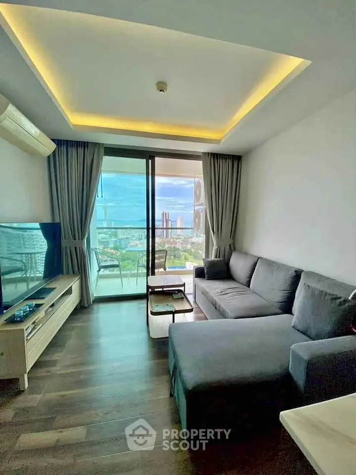 Modern living room with large window and city view, featuring a cozy gray sofa and sleek TV setup.