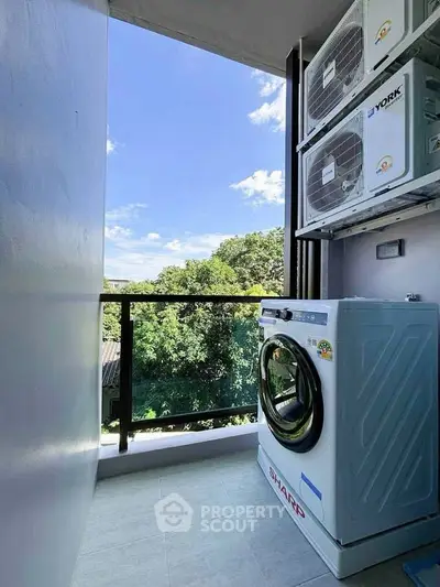 Modern balcony with washing machine and air conditioning units, offering a serene green view.
