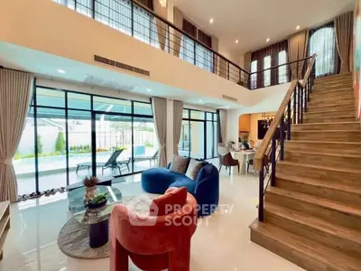 Luxurious modern living room with high ceilings, elegant staircase, and large windows overlooking a garden.