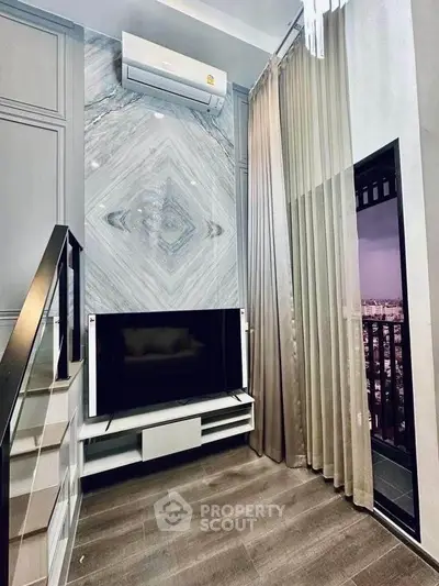 Modern living room with stylish decor and city view balcony, featuring sleek TV setup and elegant curtains.