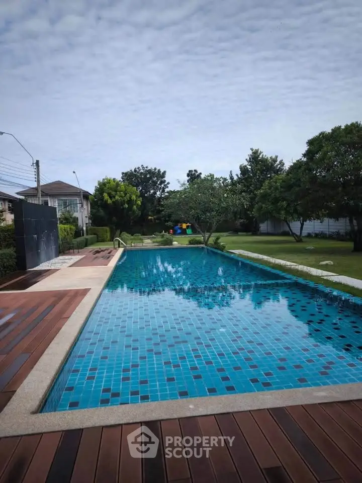 Luxurious outdoor pool with wooden deck and lush garden in serene residential area.