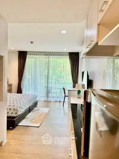 Modern studio apartment with large windows and balcony overlooking greenery, featuring sleek furnishings and open layout.