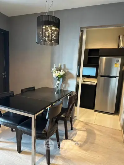 Modern dining area with sleek black table and chairs, adjacent to a compact kitchen with stainless steel appliances.