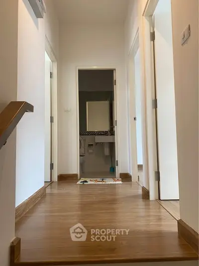 Bright hallway with wooden flooring leading to a modern bathroom, showcasing sleek interior design.