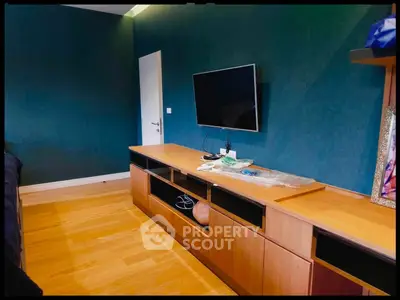 Modern living room with sleek wooden furniture and mounted TV, featuring elegant teal walls.