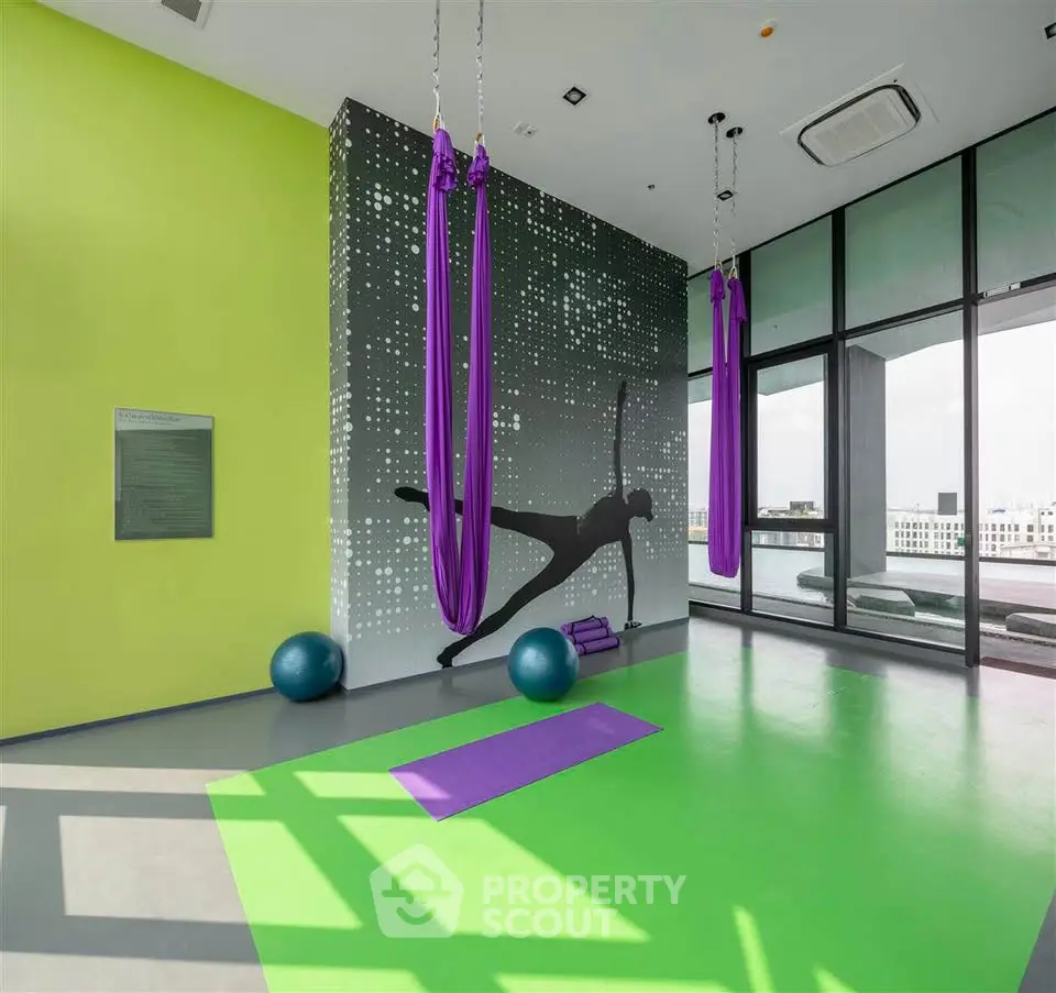 Modern gym with aerial yoga setup and city view, featuring vibrant green and purple decor.