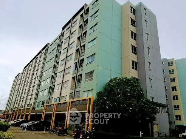 Modern multi-story apartment building with parking area and lush greenery.