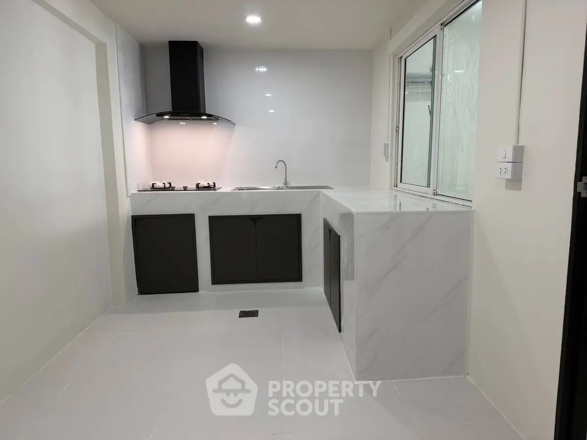 Modern kitchen with sleek black cabinets and marble countertops, featuring a gas stove and ample natural light.