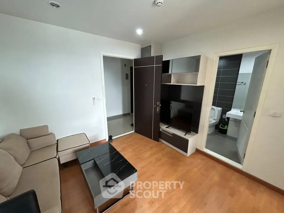 Modern living room with sleek furniture and wooden flooring, adjacent to a stylish bathroom.