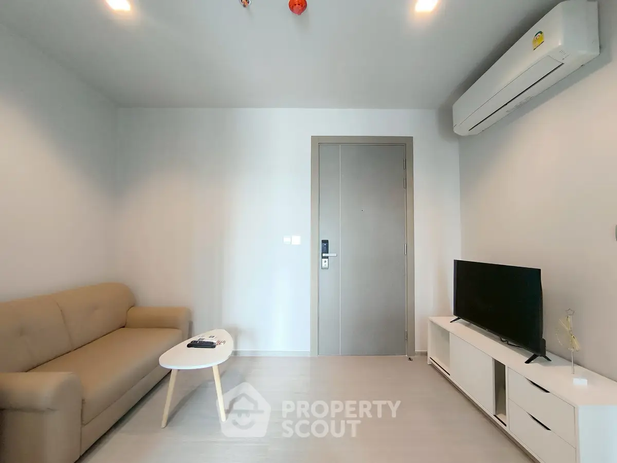 Modern living room with beige sofa, flat-screen TV, and air conditioning unit.