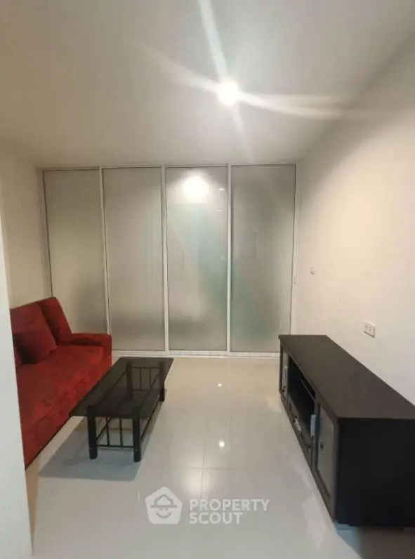 Modern living room with red sofa and glass sliding doors in a minimalist apartment.