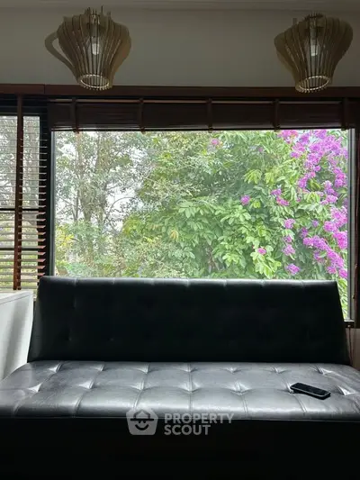 Charming living room with large window view of lush garden and stylish lighting fixtures.