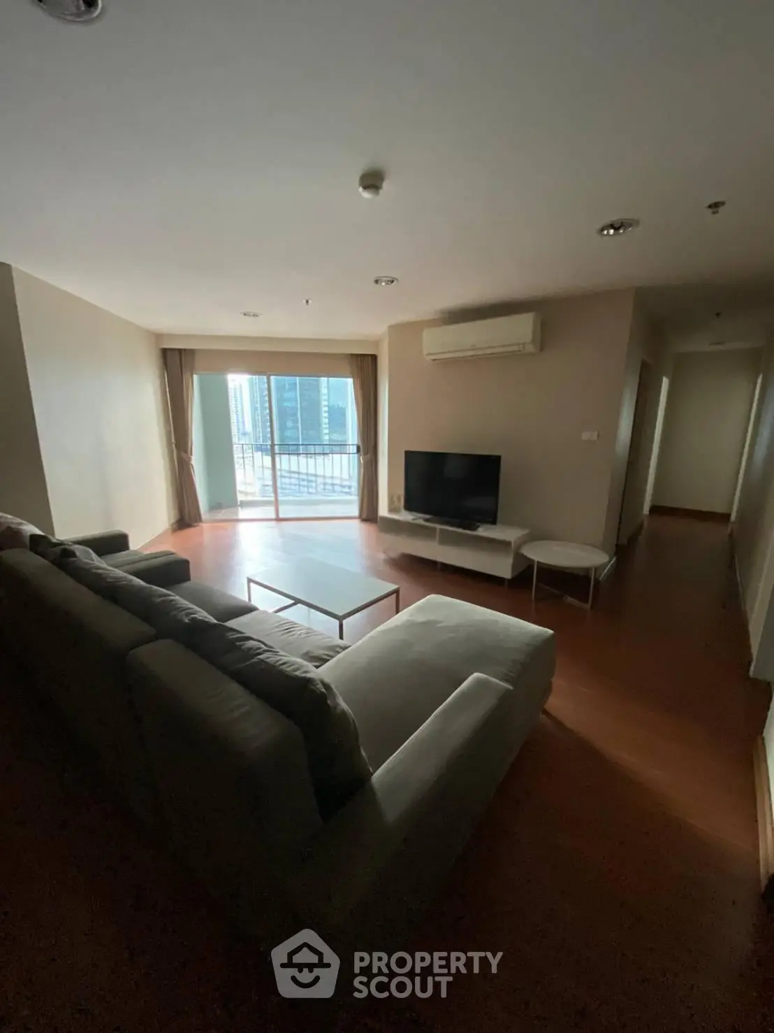 Spacious living room with modern sofa and city view balcony in high-rise apartment.