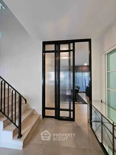 Modern interior with sleek staircase and glass partition leading to a cozy living area.