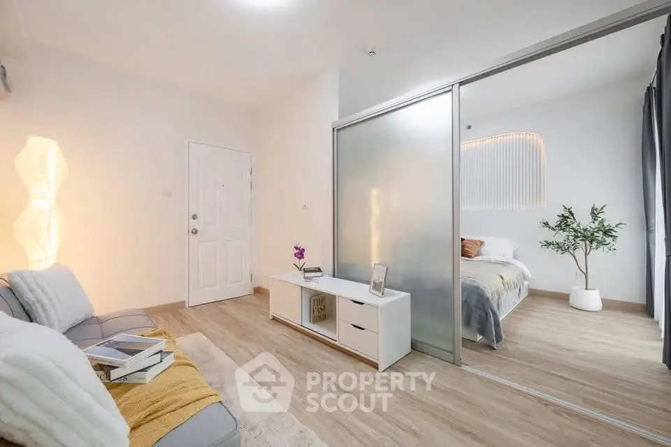 Modern living room with sliding glass door to cozy bedroom, stylish decor and warm lighting.
