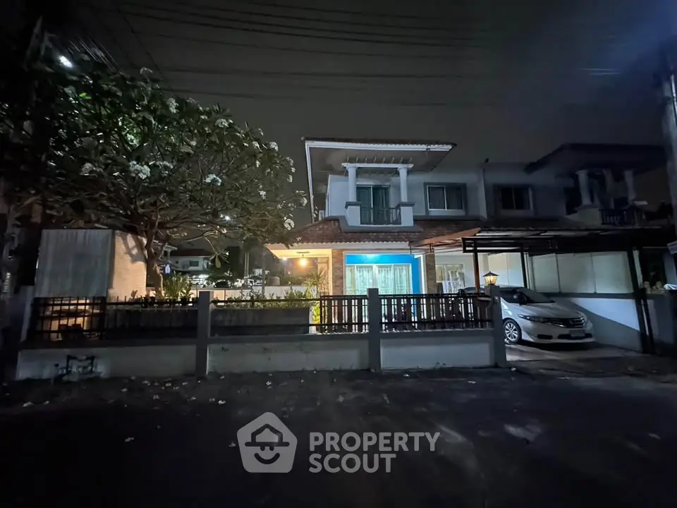 Charming two-story house with carport and garden, illuminated at night, perfect for family living.