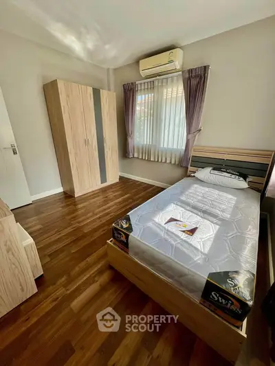 Modern bedroom with wooden flooring, single bed, and wardrobe, featuring natural light and air conditioning.