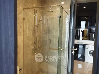 Modern bathroom with glass shower and washing machine in sleek apartment.