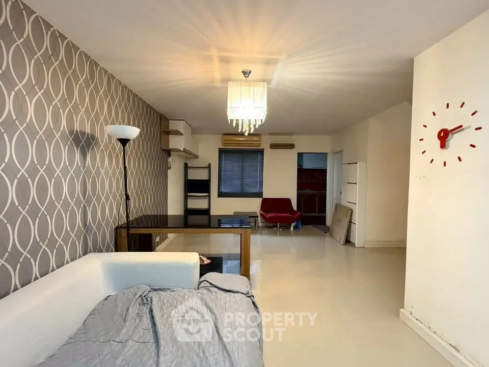 Spacious living room with modern decor and stylish wallpaper, featuring a chic chandelier and cozy seating area.