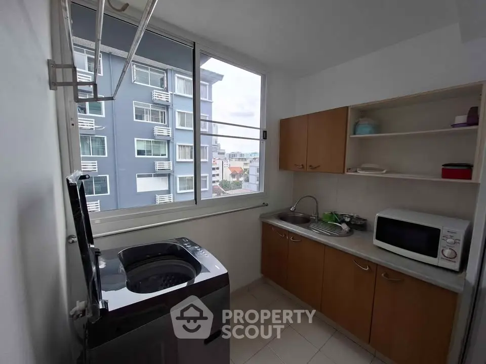 Modern kitchen with washing machine and microwave, featuring ample natural light and urban view.