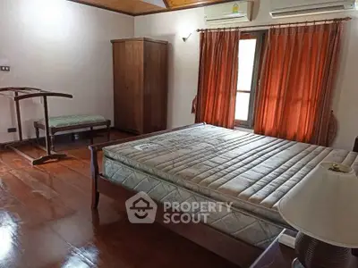 Spacious bedroom with wooden flooring and natural light, featuring a large bed and elegant curtains.