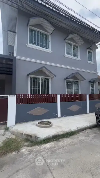 Charming two-story gray house with decorative windows and secure fencing in a quiet neighborhood.