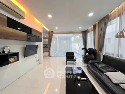 Modern living room with sleek black leather sofa and large windows for natural light.