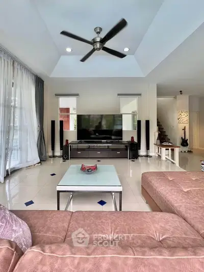 Spacious living room with modern decor and ceiling fan, featuring a large TV and comfortable seating.