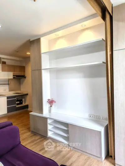 Modern living room with built-in shelving and stylish kitchen in open layout apartment.