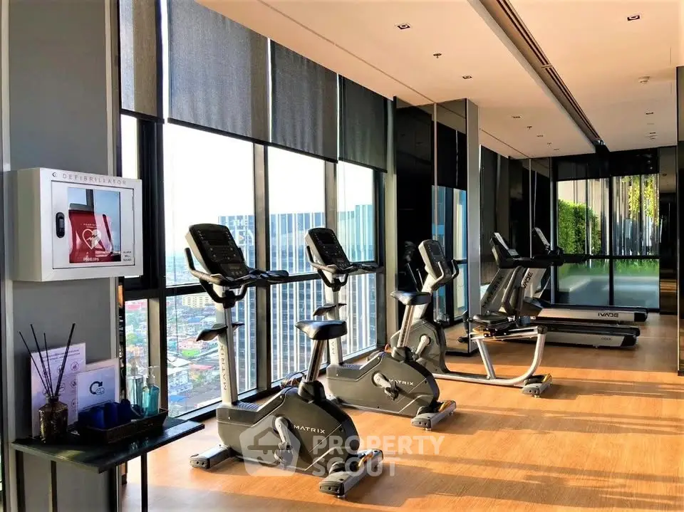 Modern gym with exercise bikes and treadmill in a high-rise building with city views.