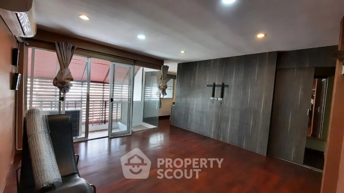 Spacious living room with wooden flooring and large windows leading to a balcony.