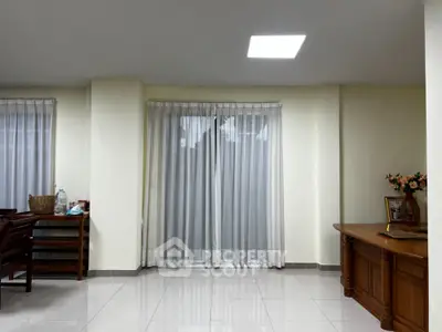 Spacious and well-lit living area with gleaming tiled floors, elegant sheer curtains, and classic wooden furniture, perfect for modern living.
