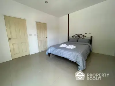 Spacious bedroom with ample natural light, featuring a large bed, tiled flooring, and two wooden doors leading to other rooms.