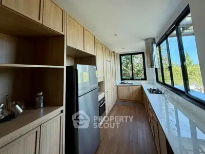 Modern kitchen with sleek wooden cabinetry and large windows offering natural light.