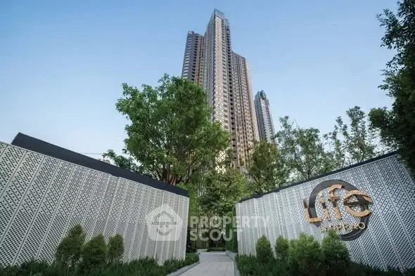 Modern high-rise building with lush greenery and stylish entrance in urban setting.