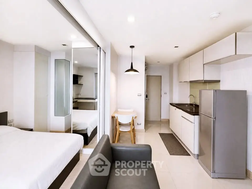 Modern studio apartment with sleek kitchen and cozy living area, featuring mirrored wardrobe and stylish decor.