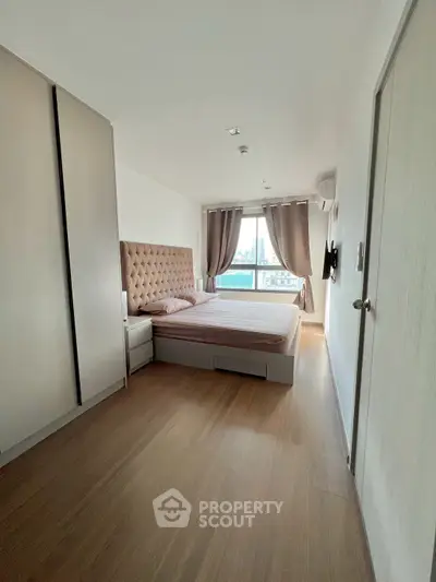 Spacious bedroom with large window and modern furnishings in a high-rise apartment.