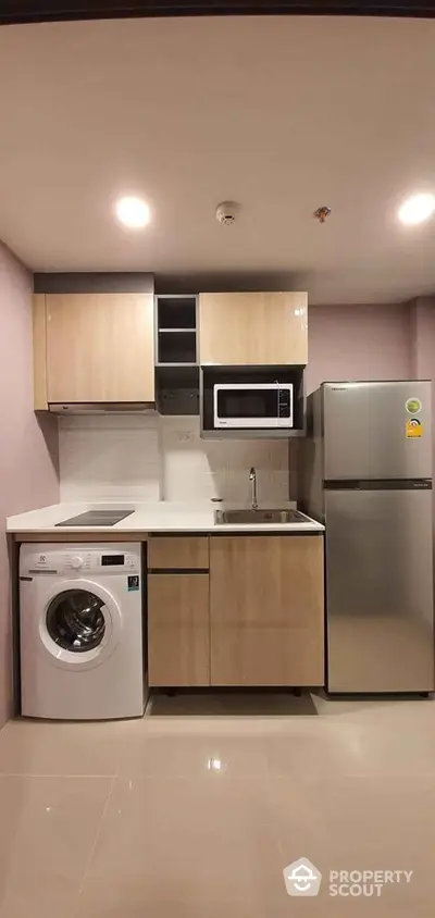 Modern compact kitchen with washing machine, microwave, and fridge in sleek apartment.