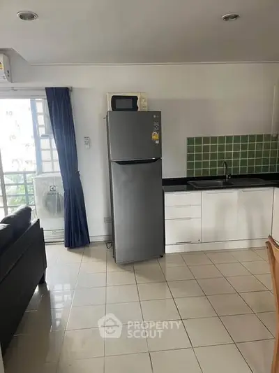 Modern kitchen with stainless steel fridge and green tile backsplash in a bright apartment.